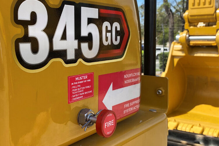 Red Muster FIRE actuation button and instruction decal on the side of a Caterpillar 345 GC excavator